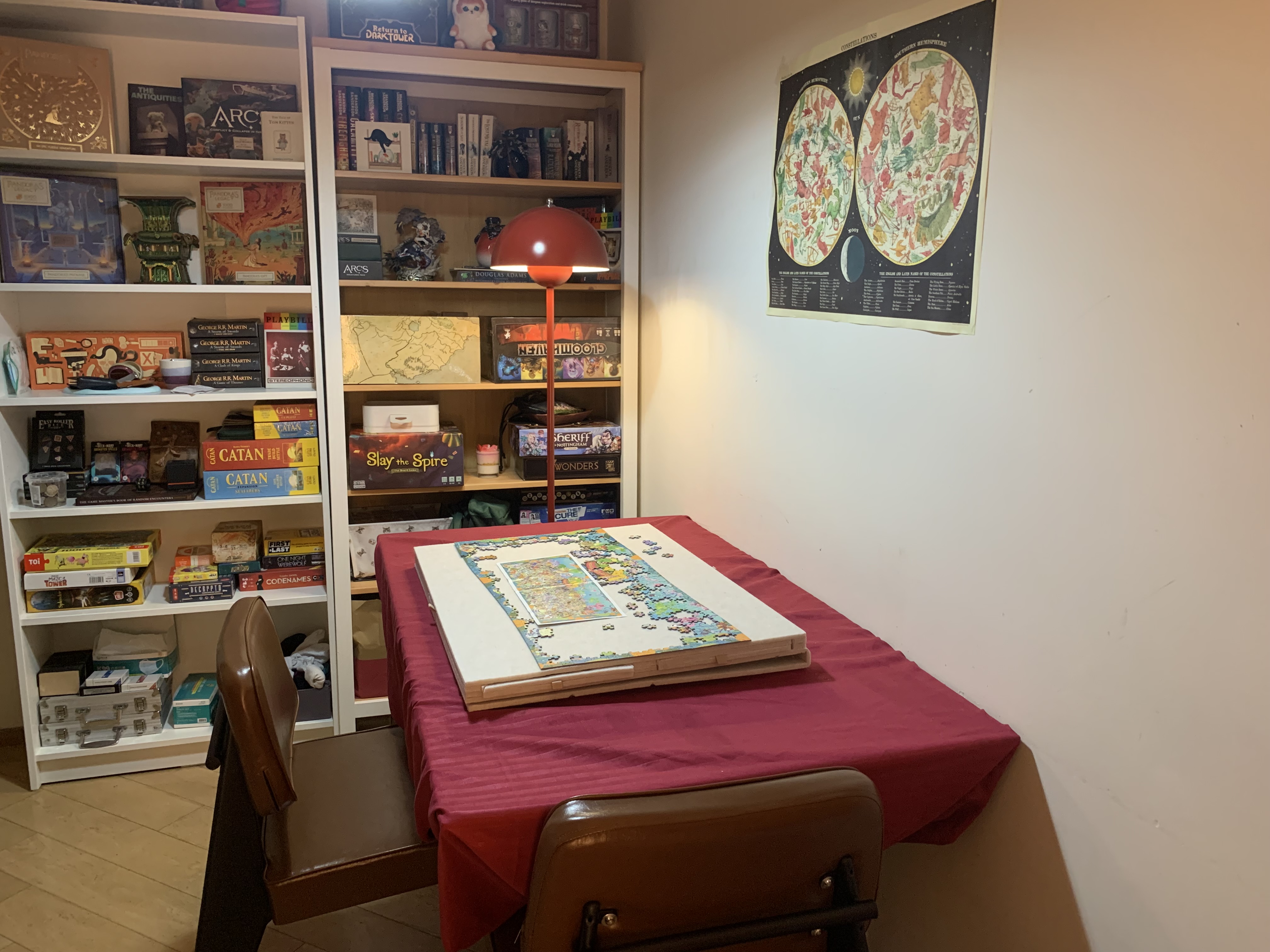 A small apartment board game and puzzle area with a dining table used for multiple activities, surrounded by shelves of games and books.